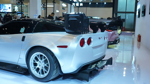 Close-up of a silver wide-body Chevrolet Corvette performance car displayed indoors, featuring aggressive aerodynamic bodywork, carbon fiber front splitter, vented hood, and lightweight multi-spoke wheels. The image highlights the custom motorsport styling and premium carbon fiber aero components under exhibition lighting.