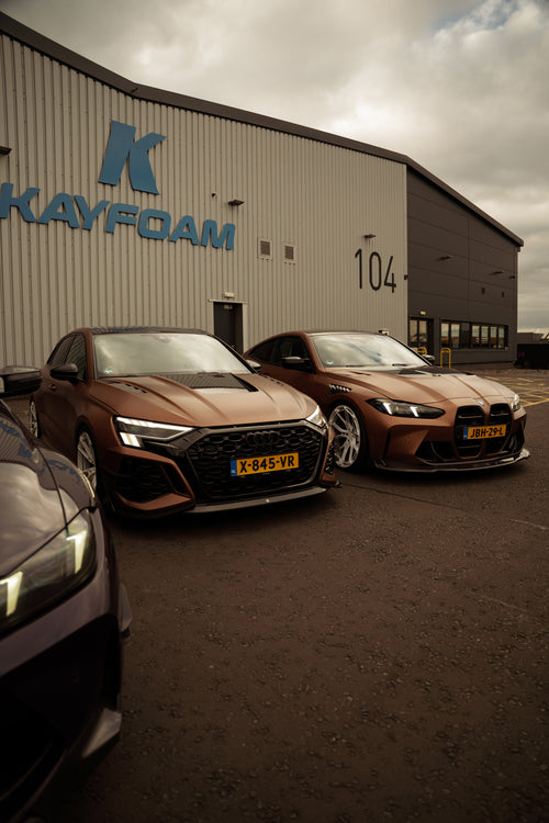Bronze Audi RS4 Avant featuring a REVOZPORT carbon fiber body kit with front lip and side skirts, paired with silver multi-spoke forged wheels, parked in a modern urban setting.