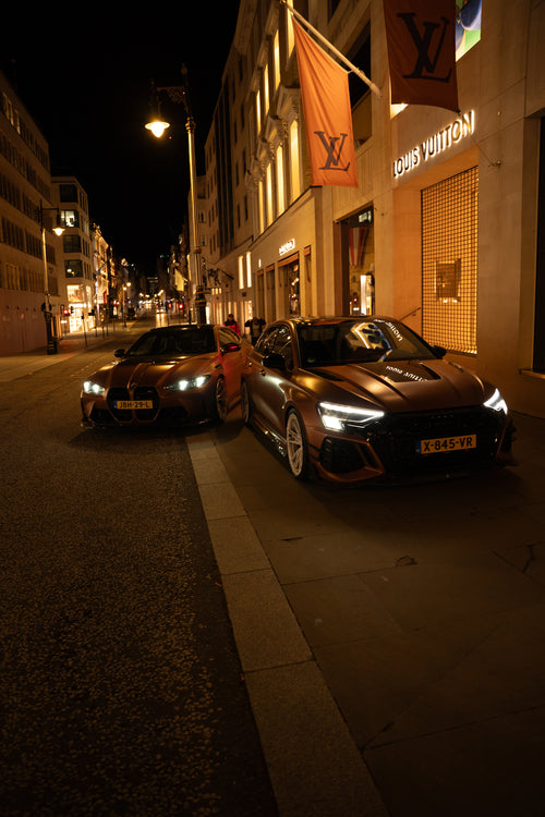 Bronze Audi RS4 Avant featuring a REVOZPORT carbon fiber body kit with front lip and side skirts, paired with silver multi-spoke forged wheels, parked in a modern urban setting.