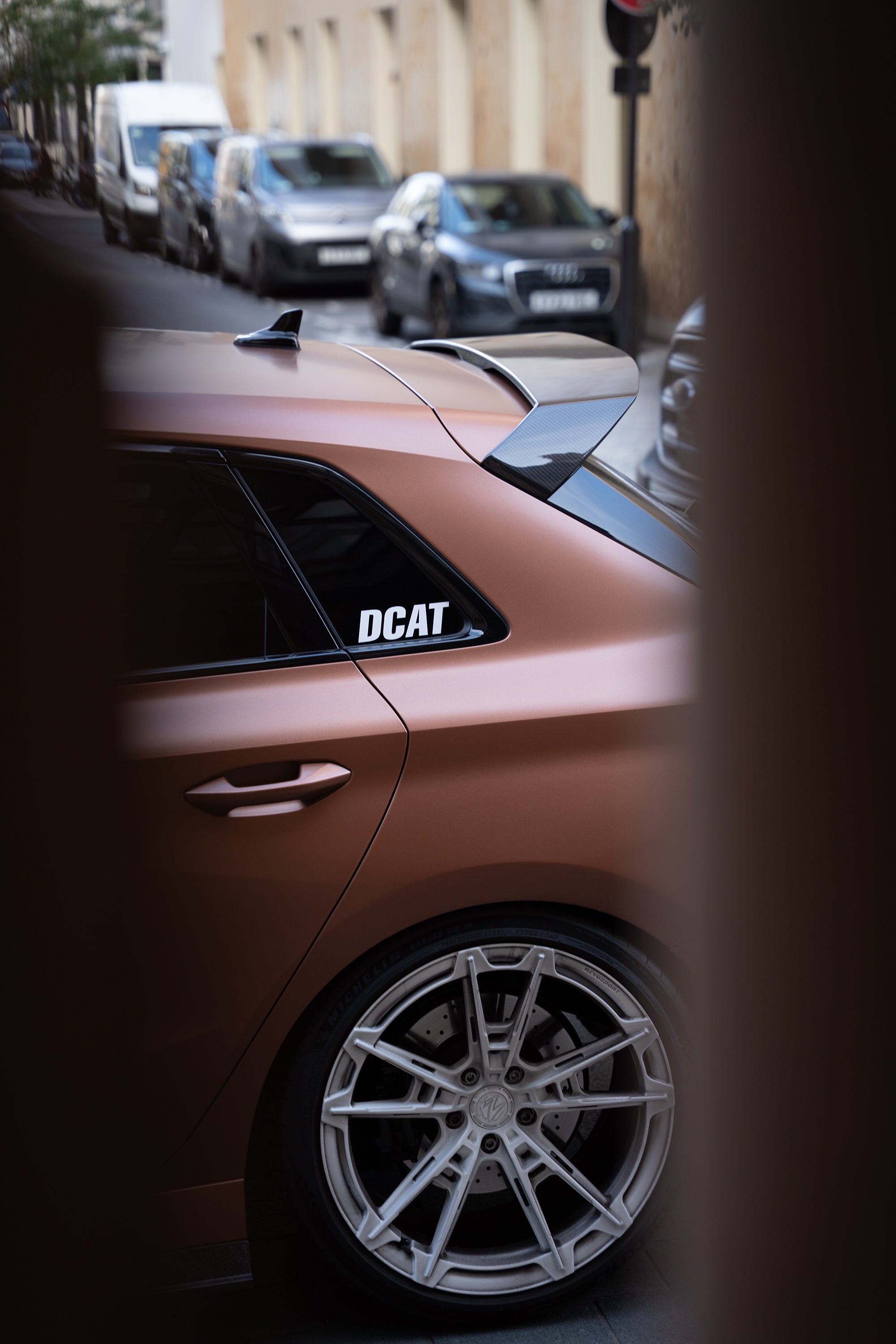 Bronze Audi RS4 Avant featuring a REVOZPORT carbon fiber body kit with front lip and side skirts, paired with silver multi-spoke forged wheels, parked in a modern urban setting.