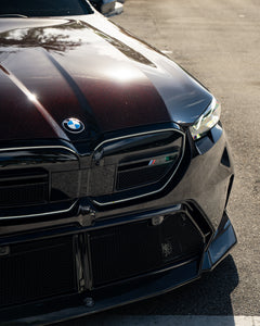 BMW touring car with carbon fiber body kit parked in a leafy outdoor lot, highlighting front lip and lowered stance.