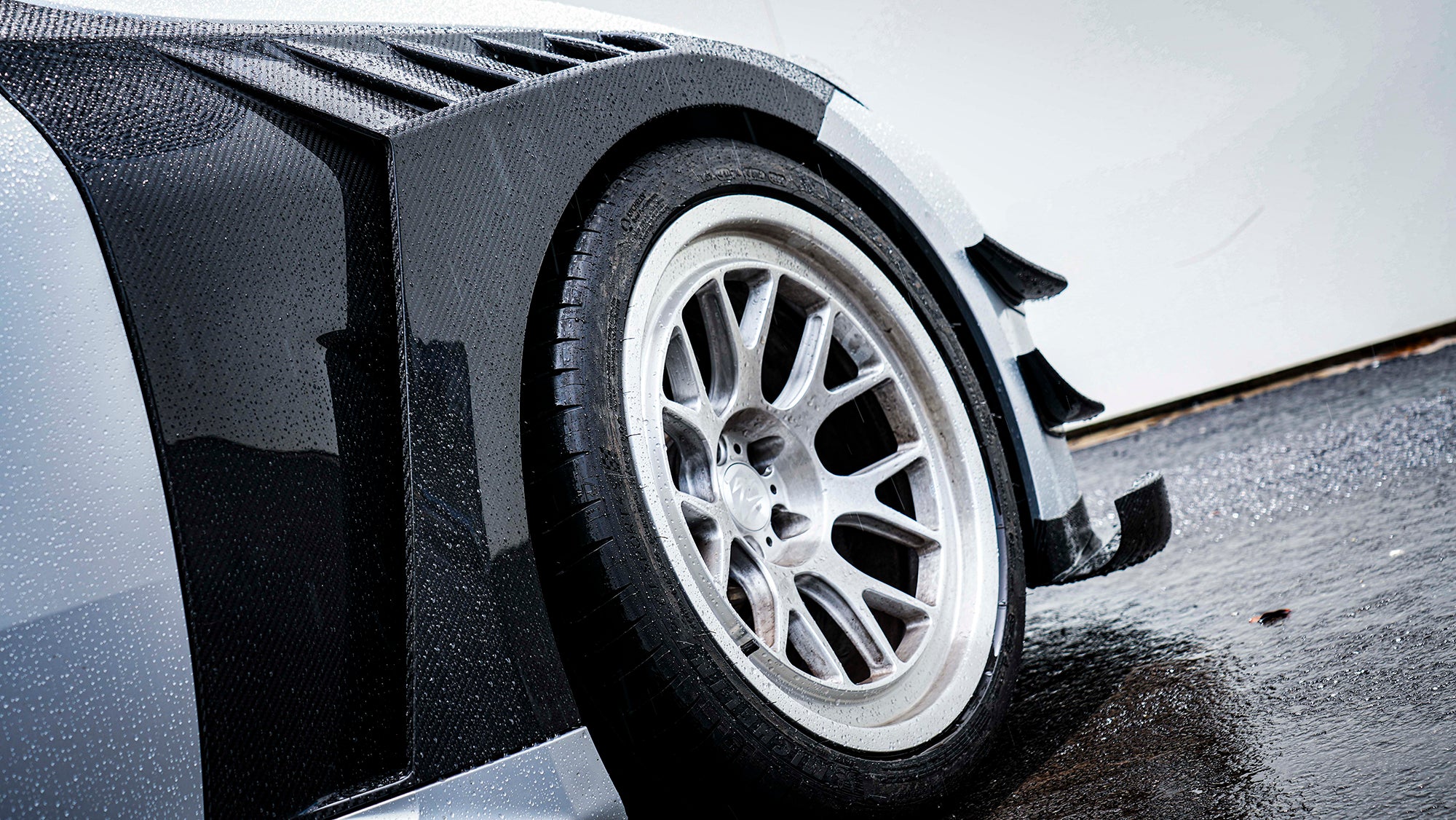 Close-up of a white wheel and carbon fiber widebody fender, highlighting aggressive aero styling and detailed craftsmanship.