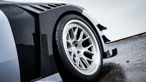 Close-up of a white wheel and carbon fiber widebody fender, highlighting aggressive aero styling and detailed craftsmanship.