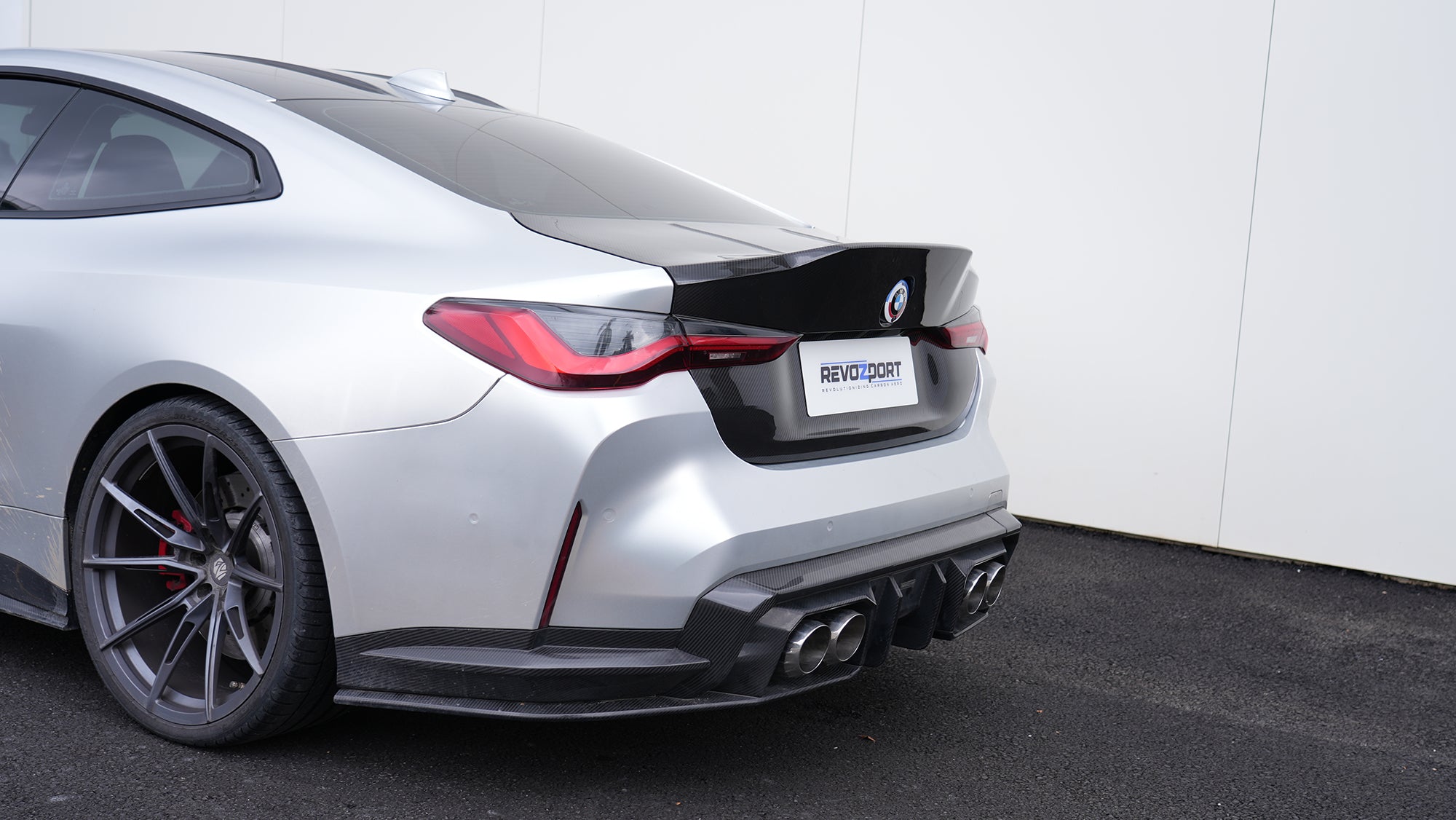 Close-up of a BMW G82 M4 rear end featuring a REVOZPORT carbon fiber trunk lid and integrated carbon rear spoiler, highlighting the glossy carbon weave detail.