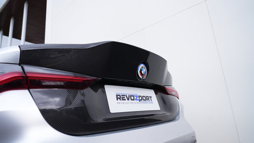 Close-up of a BMW G82 M4 rear end featuring a REVOZPORT carbon fiber trunk lid and integrated carbon rear spoiler, highlighting the glossy carbon weave detail.