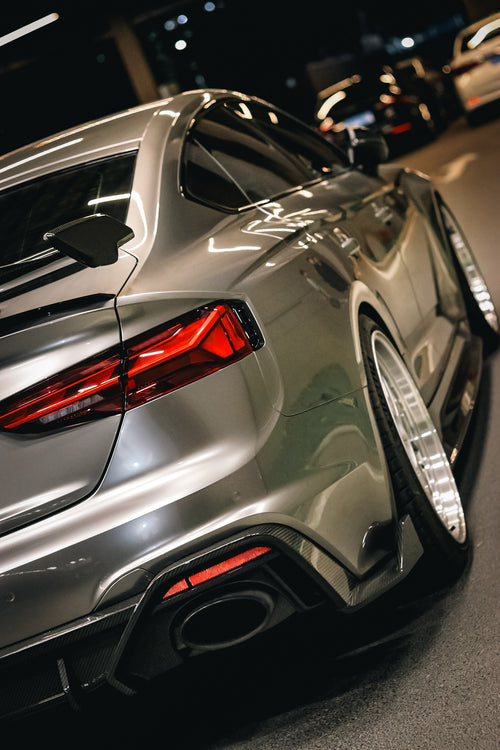 Top-down view of a gray Audi RS5 Sportback featuring a REVOZPORT carbon fiber body kit with vented hood, front lip, side skirts, and large rear wing driving through a dimly lit urban tunnel at night.