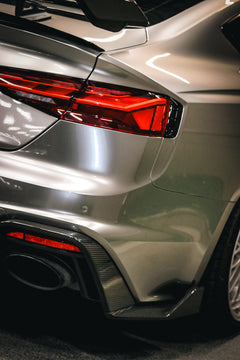Top-down view of a gray Audi RS5 Sportback featuring a REVOZPORT carbon fiber body kit with vented hood, front lip, side skirts, and large rear wing driving through a dimly lit urban tunnel at night.
