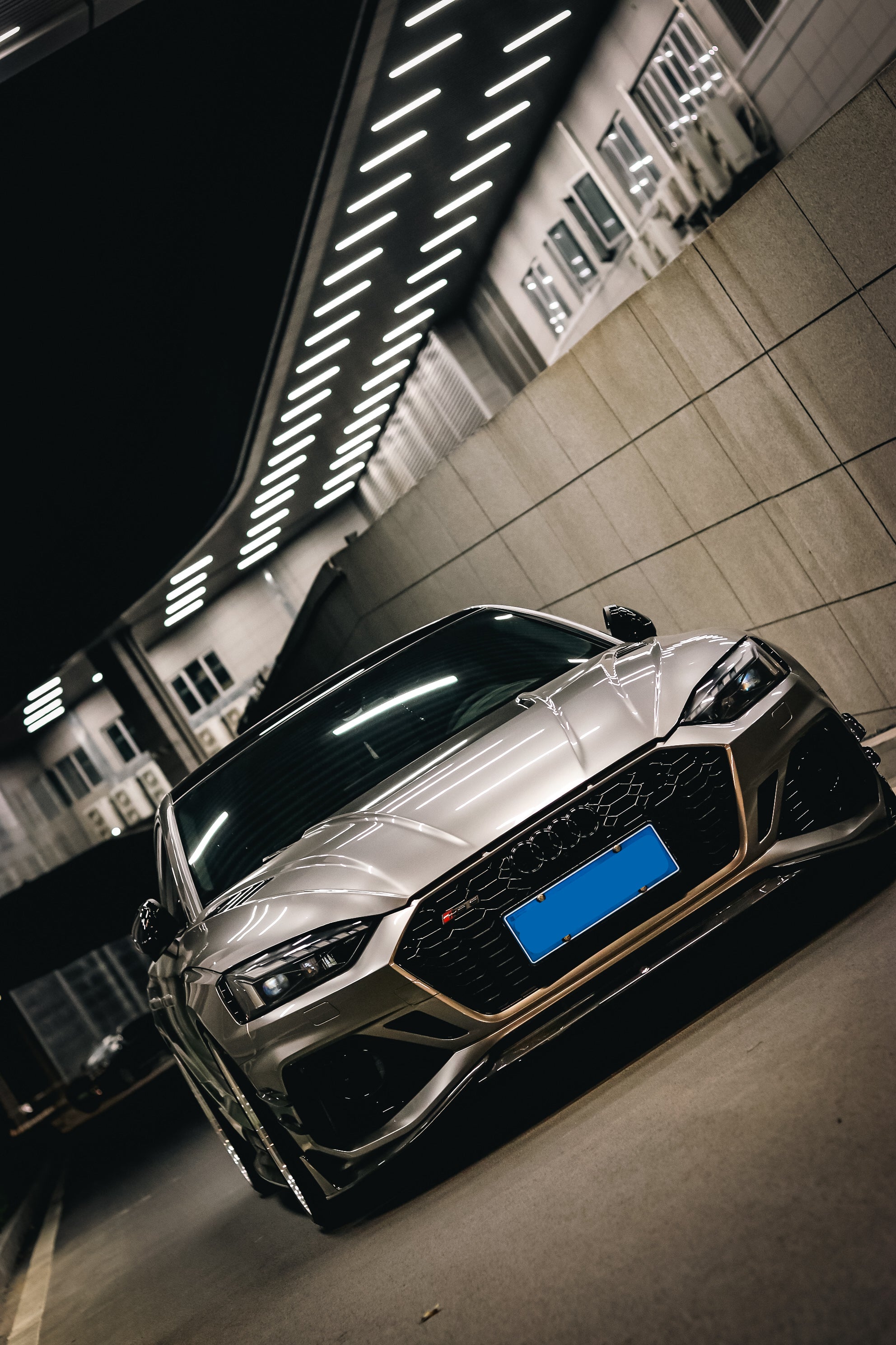 Top-down view of a gray Audi RS5 Sportback featuring a REVOZPORT carbon fiber body kit with vented hood, front lip, side skirts, and large rear wing driving through a dimly lit urban tunnel at night.