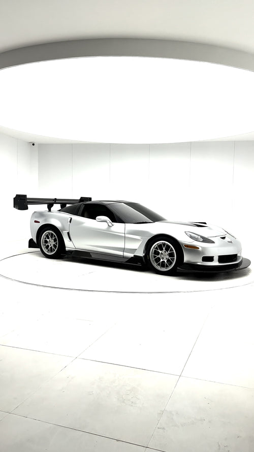 Close-up of a silver wide-body Chevrolet Corvette performance car displayed indoors, featuring aggressive aerodynamic bodywork, carbon fiber front splitter, vented hood, and lightweight multi-spoke wheels. The image highlights the custom motorsport styling and premium carbon fiber aero components under exhibition lighting.
