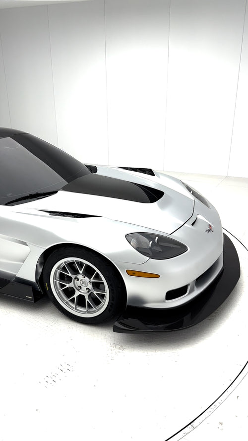 Close-up of a silver wide-body Chevrolet Corvette performance car displayed indoors, featuring aggressive aerodynamic bodywork, carbon fiber front splitter, vented hood, and lightweight multi-spoke wheels. The image highlights the custom motorsport styling and premium carbon fiber aero components under exhibition lighting.