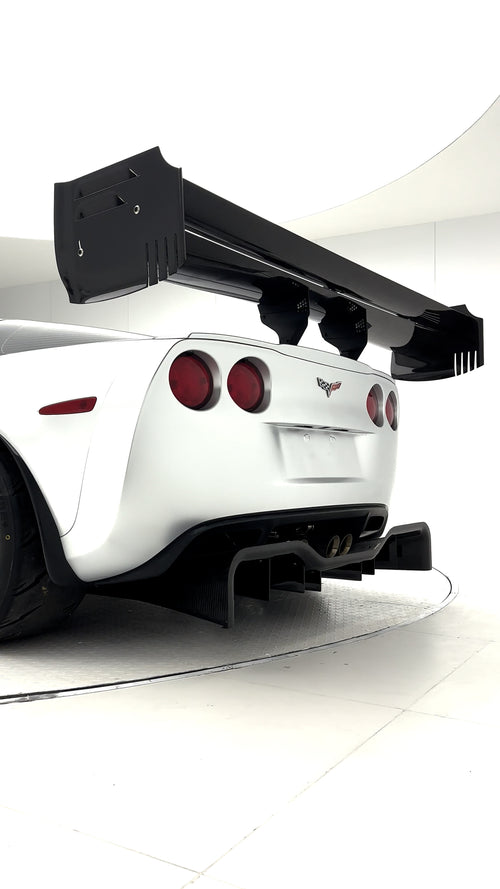 Close-up of a silver wide-body Chevrolet Corvette performance car displayed indoors, featuring aggressive aerodynamic bodywork, carbon fiber front splitter, vented hood, and lightweight multi-spoke wheels. The image highlights the custom motorsport styling and premium carbon fiber aero components under exhibition lighting.