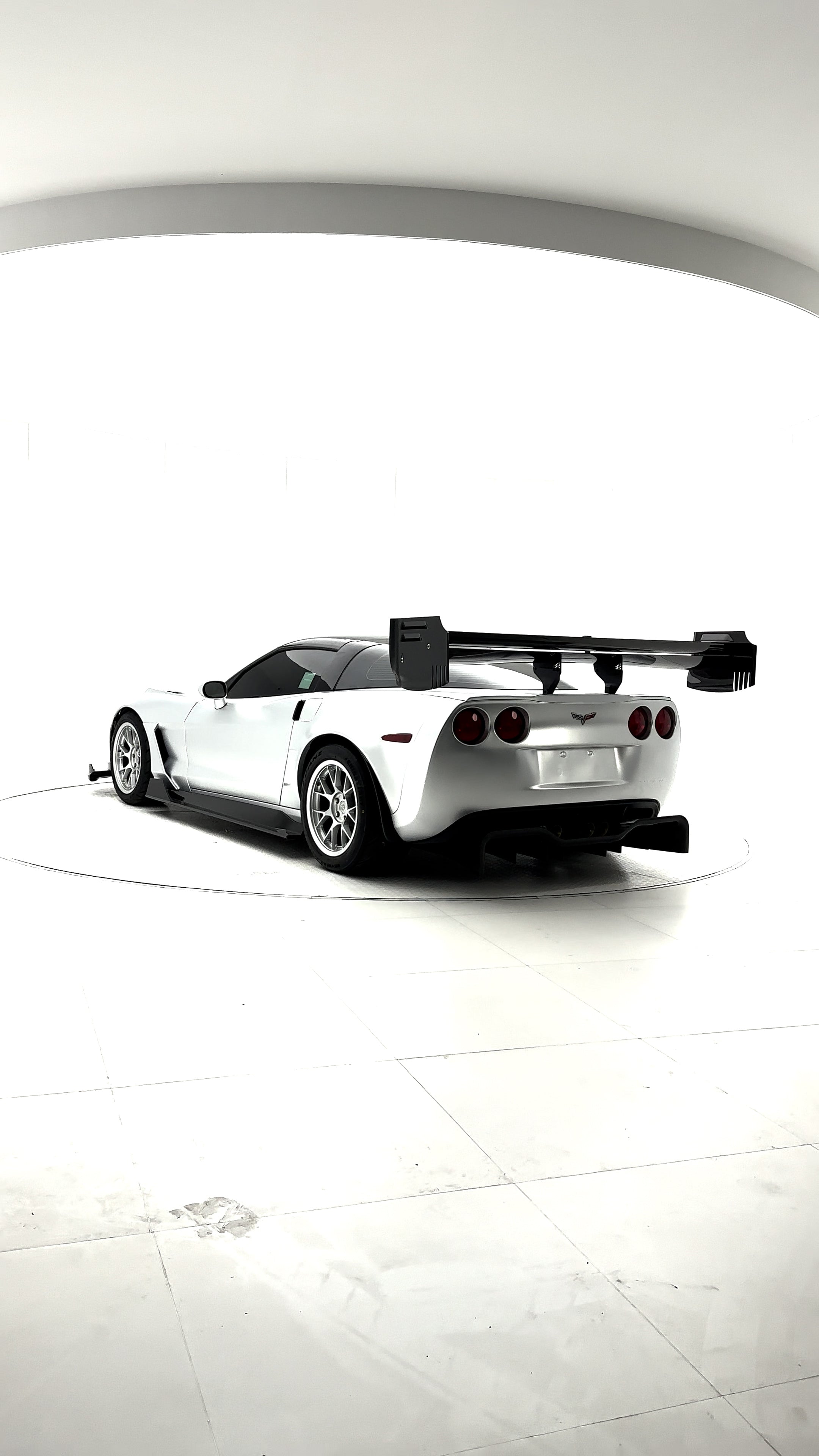 Close-up of a silver wide-body Chevrolet Corvette performance car displayed indoors, featuring aggressive aerodynamic bodywork, carbon fiber front splitter, vented hood, and lightweight multi-spoke wheels. The image highlights the custom motorsport styling and premium carbon fiber aero components under exhibition lighting.