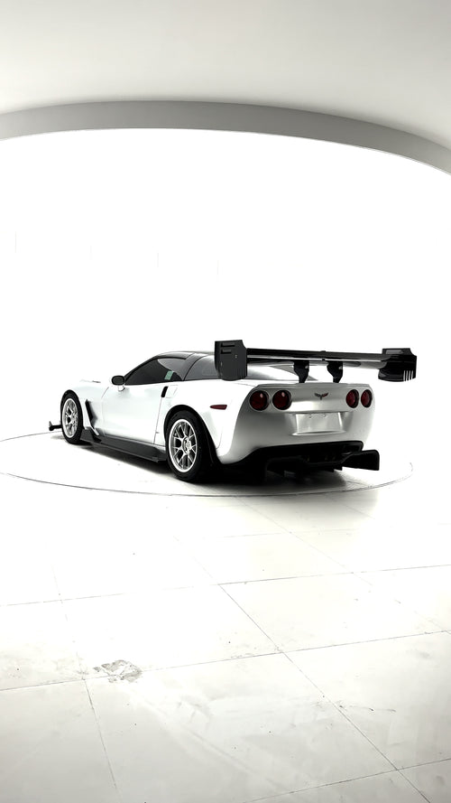 Close-up of a silver wide-body Chevrolet Corvette performance car displayed indoors, featuring aggressive aerodynamic bodywork, carbon fiber front splitter, vented hood, and lightweight multi-spoke wheels. The image highlights the custom motorsport styling and premium carbon fiber aero components under exhibition lighting.