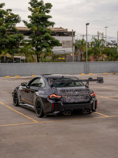 Gray BMW M2 featuring a REVOZPORT body kit with front lip, rear wing, canards, vented fenders, and hood, parked in an open rooftop lot.