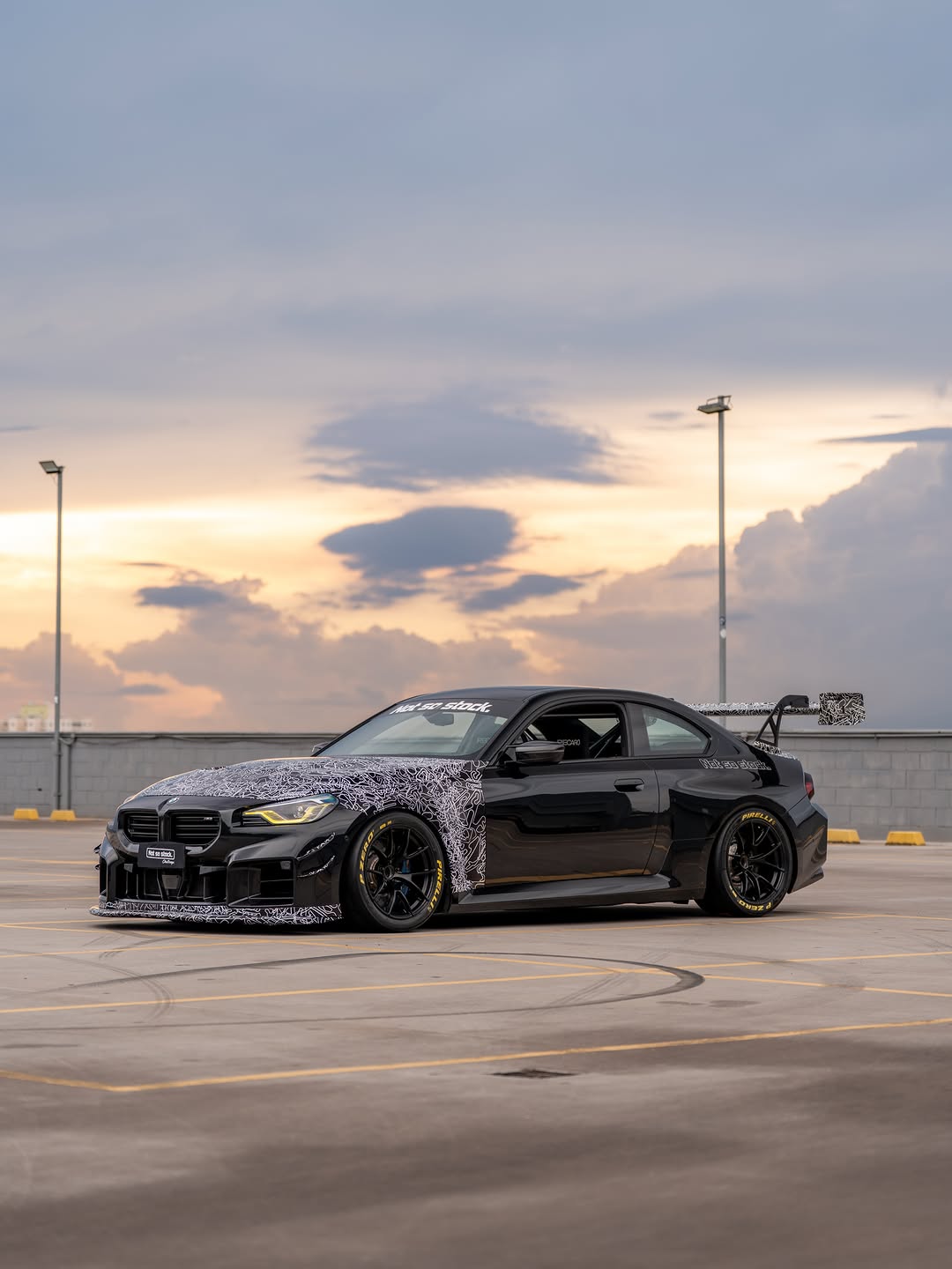 Gray BMW M2 featuring a REVOZPORT body kit with front lip, rear wing, canards, vented fenders, and hood, parked in an open rooftop lot.