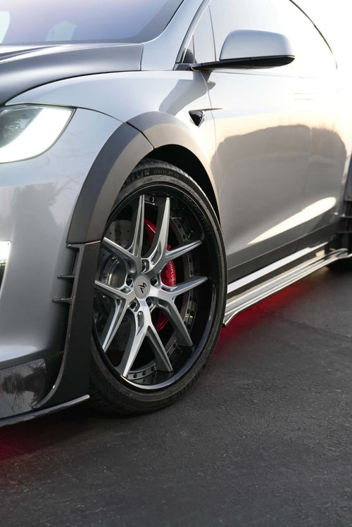 Tesla Model X featuring an aggressive REVOZPORT carbon fiber body kit with front lip, vented hood, wide fender extensions, side skirts, and illuminated red underglow lighting at dusk.
