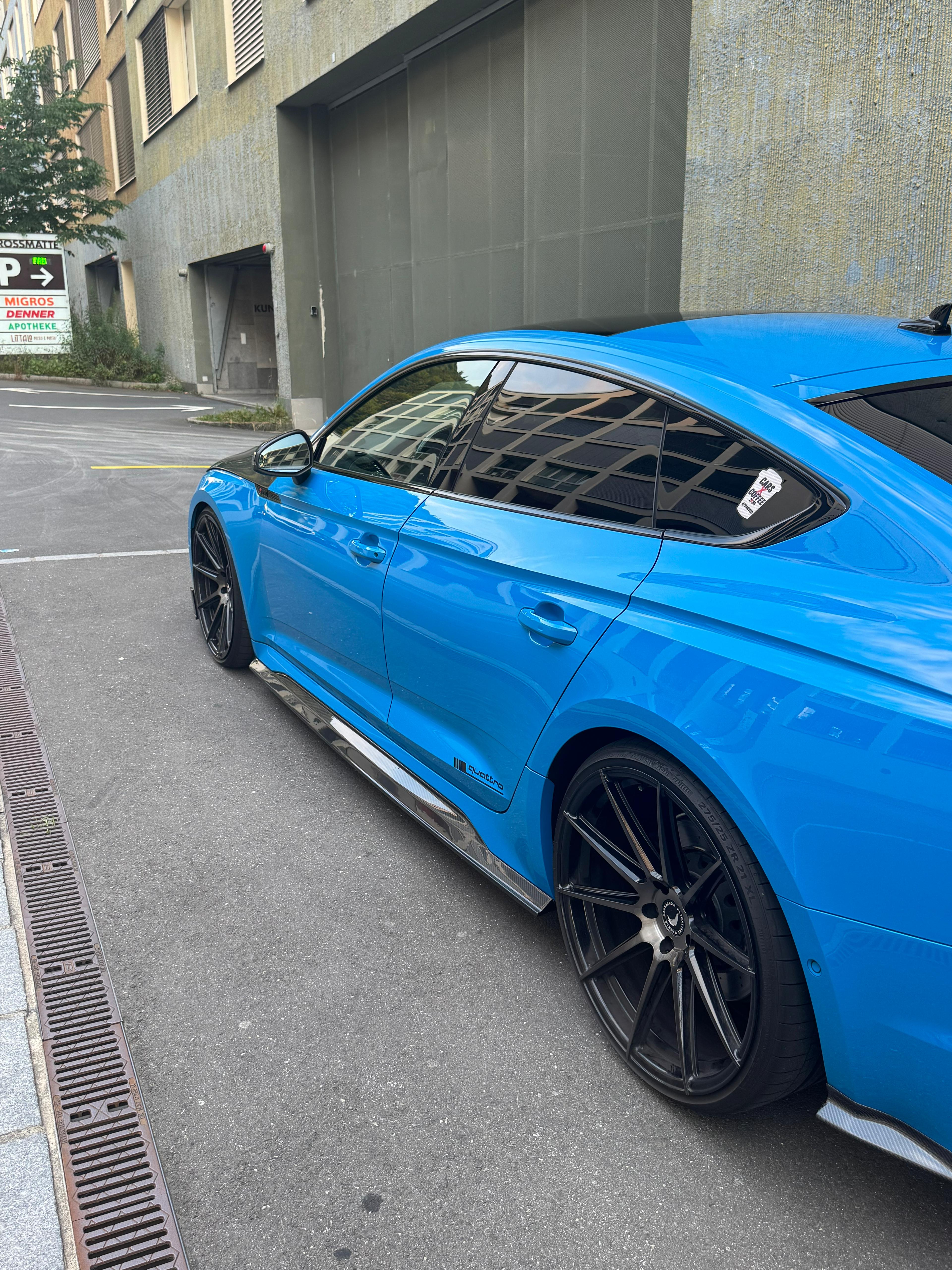 Blue Audi RS5 Sportback featuring a REVOZPORT carbon fiber body kit with vented hood, front lip, side skirts, and lowered stance parked outside a modern industrial building at sunset.