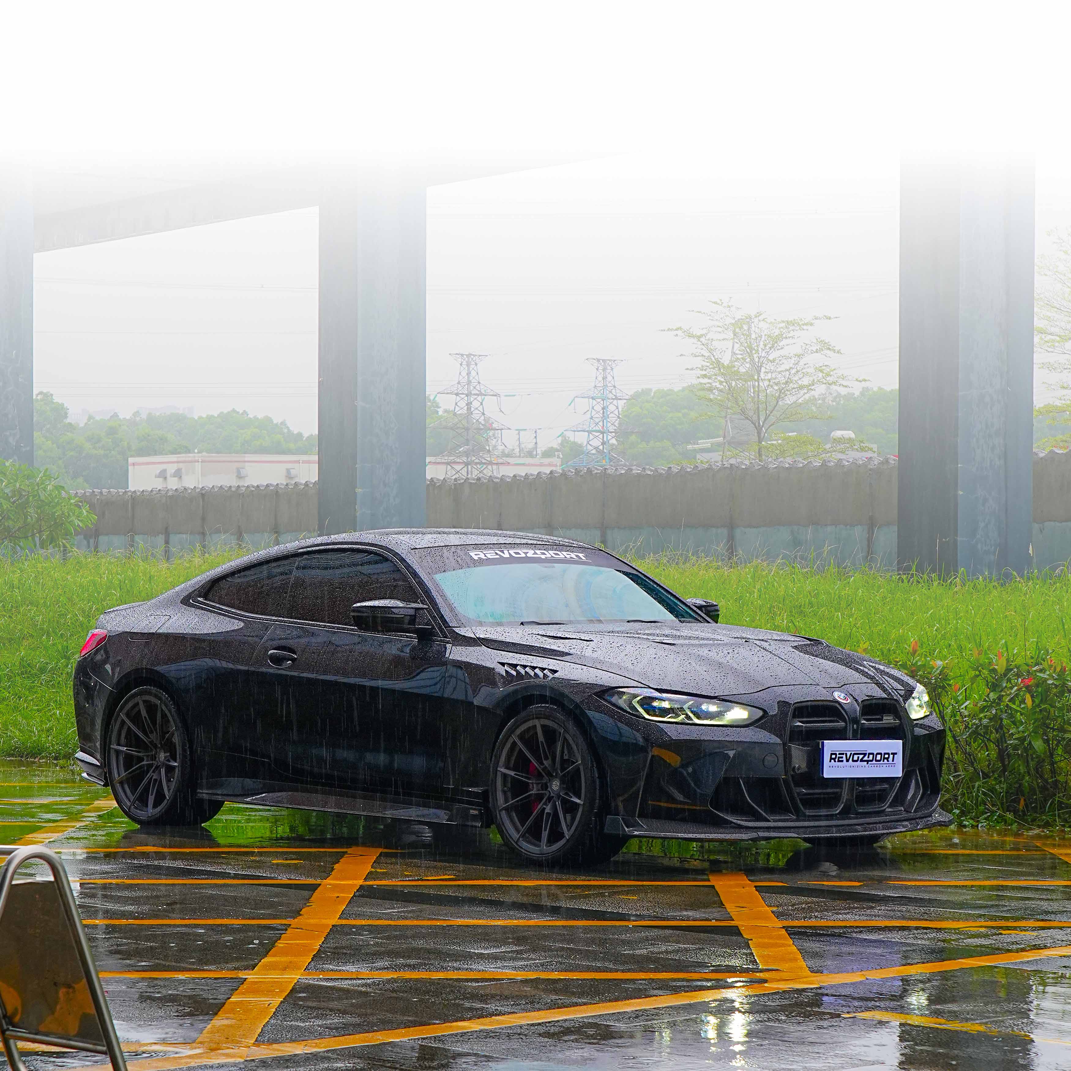Black BMW car parked in a wet parking lot with grass and trees in the background.