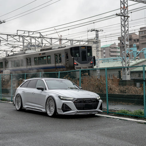 White Audi RS6 Avant featuring a REVOZPORT carbon fiber body kit with front lip, side skirts, rear diffuser, and lowered stance driving at high speed on a highway.