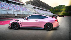 Pink BMW G82 M4 fitted with a REVOZPORT carbon fiber widebody aero kit, front splitter, hood vents, and side skirts on a race track pit lane.