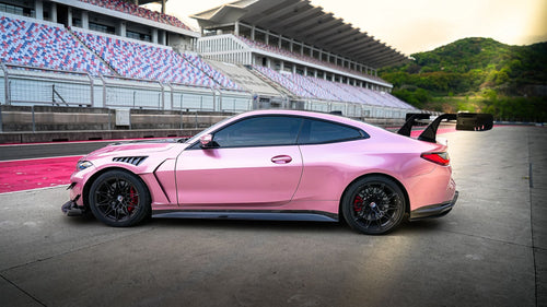 Pink BMW G82 M4 fitted with a REVOZPORT carbon fiber widebody aero kit, front splitter, hood vents, and side skirts on a race track pit lane.
