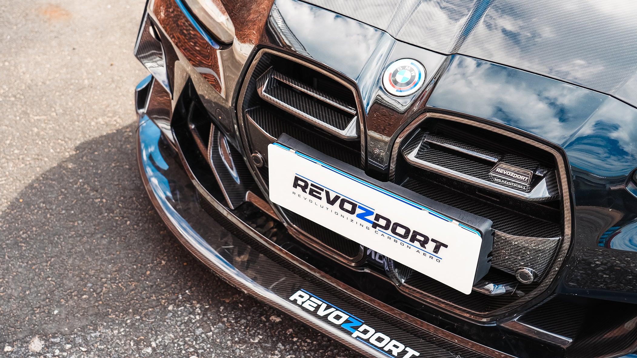 Black BMW G82 M4 track build with carbon fiber vented fenders, side skirts, rear diffuser, and oversized GT wing parked at a professional racing circuit pit lane.