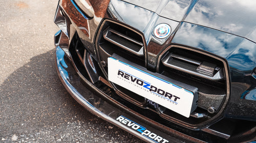 Black BMW G82 M4 track build with carbon fiber vented fenders, side skirts, rear diffuser, and oversized GT wing parked at a professional racing circuit pit lane.