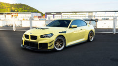Front three-quarter view of a BMW featuring aggressive carbon fiber aero, vented hood, bronze forged wheels, and oversized rear wing styling.