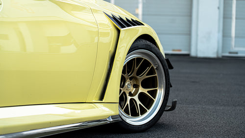 Close-up detail of a BMW widebody fender featuring carbon fiber vent accents, bronze forged wheel setup, and aggressive track-inspired styling.