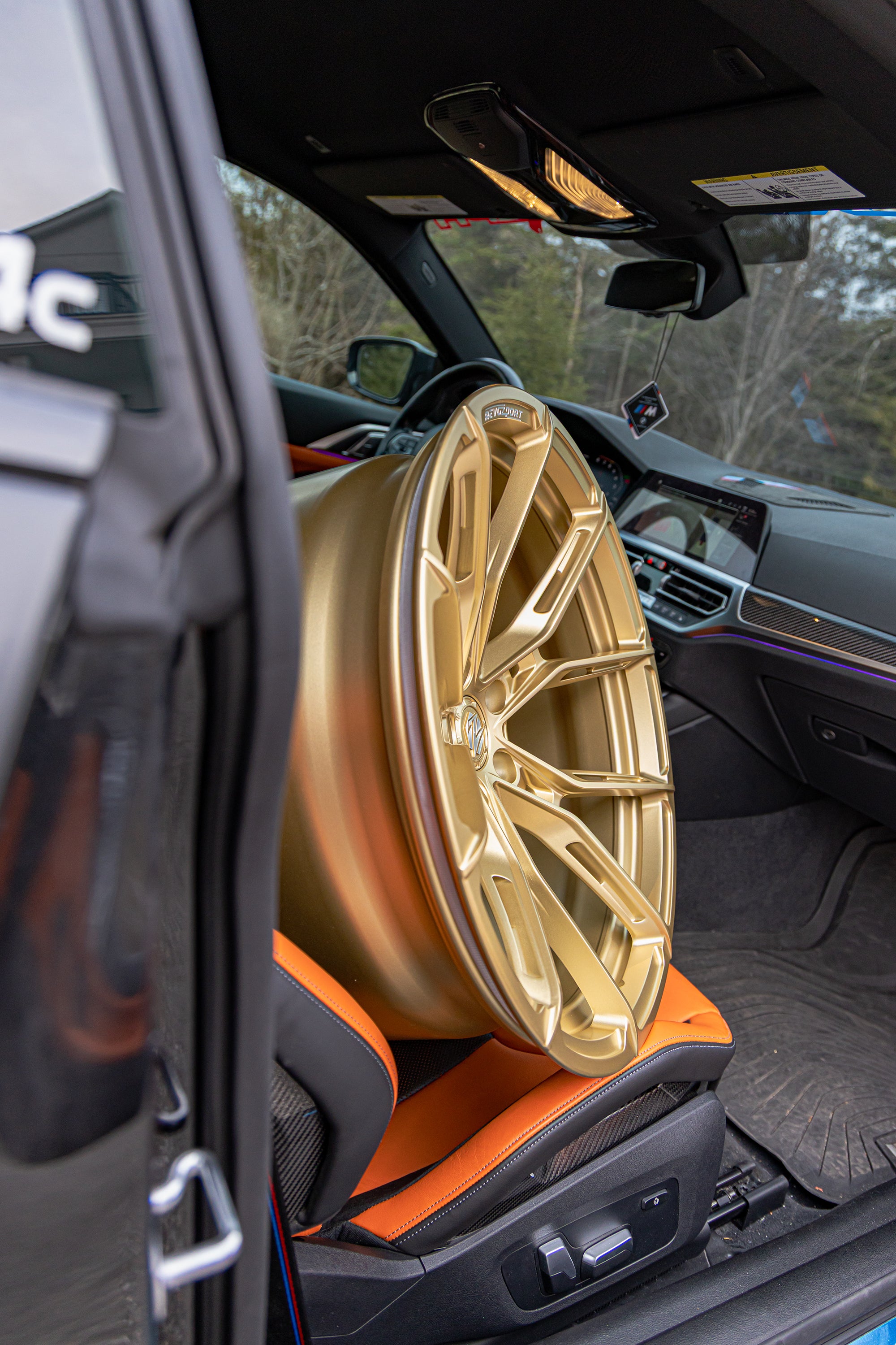 Interior detail of a BMW featuring bronze forged wheel fitment, carbon fiber cabin accents, and stripped track-focused atmosphere.