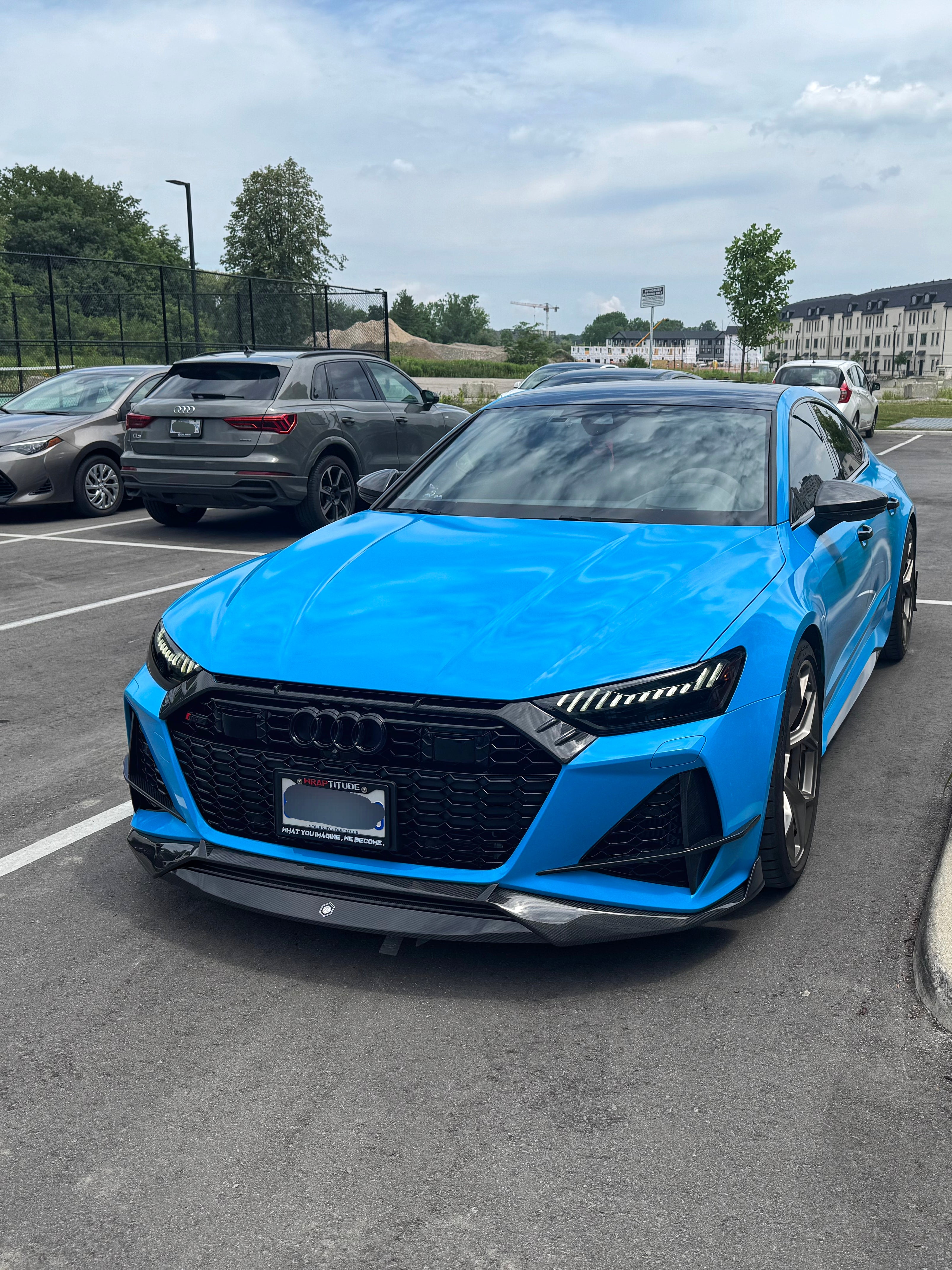 Blue Audi RS7 fitted with a REVOZPORT carbon fiber front lip and aggressive front aero styling, parked in an outdoor parking lot.