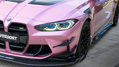 Pink BMW G82 M4 fitted with a REVOZPORT carbon fiber widebody aero kit, front splitter, hood vents, and side skirts on a race track pit lane.