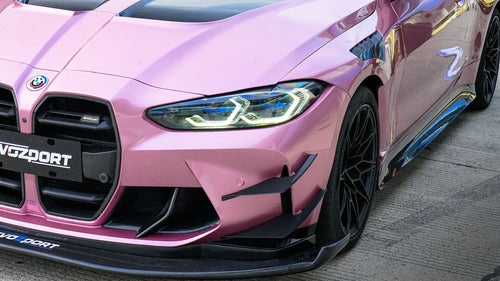 Pink BMW G82 M4 fitted with a REVOZPORT carbon fiber widebody aero kit, front splitter, hood vents, and side skirts on a race track pit lane.